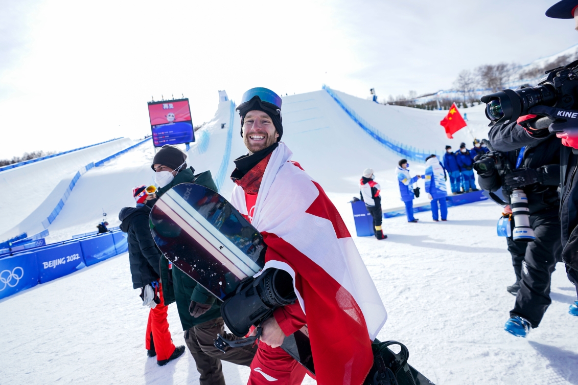 Max Parrot est tout sourire, drapé du drapeau canadien après avoir remporté la médaille d'or en slopestyle à Beijing 2022.