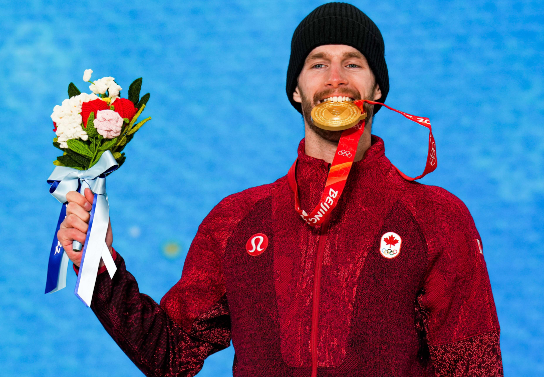 Le planchiste Max Parrot d'Équipe Canada tient sa médaille d'or de la main droite et soulève le poing gauche sur le podium du slopestyle masculin en snowboard à Beijing 2022.
