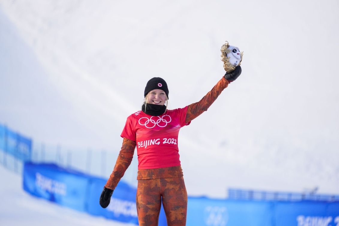 La planchiste d'Équipe Canada Meryeta O'Dine soulève la mascote des Jeux de Beijing 2022 avec sa main gauche après avoir atteint le podium de la finale du snowboard cross féminin.