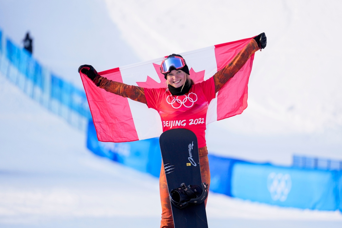 Meryeta O'Dine tient le drapeau canadien dans son dos après avoir atteint le podium du snowboard cross féminin à Beijing 2022