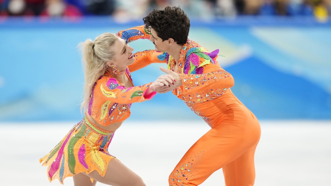 Piper Gilles et Paul Poirier performent sur la glace. Ils portent des costumes oranges et se regardent.