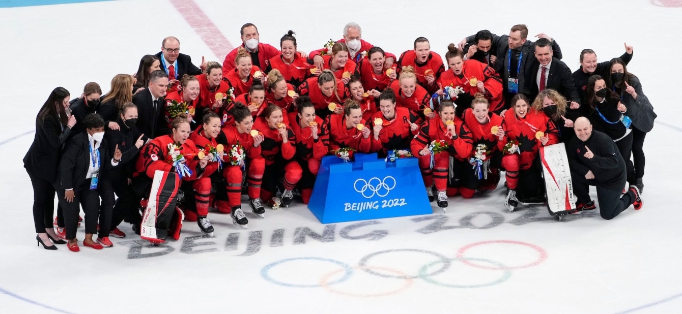 Les joueuses et les autres membres d'Équipe Canada posent pour une photo de groupe alors que les joueuses croquent leur médaille d'or gagnée en hockey féminin à Beijing 2022.