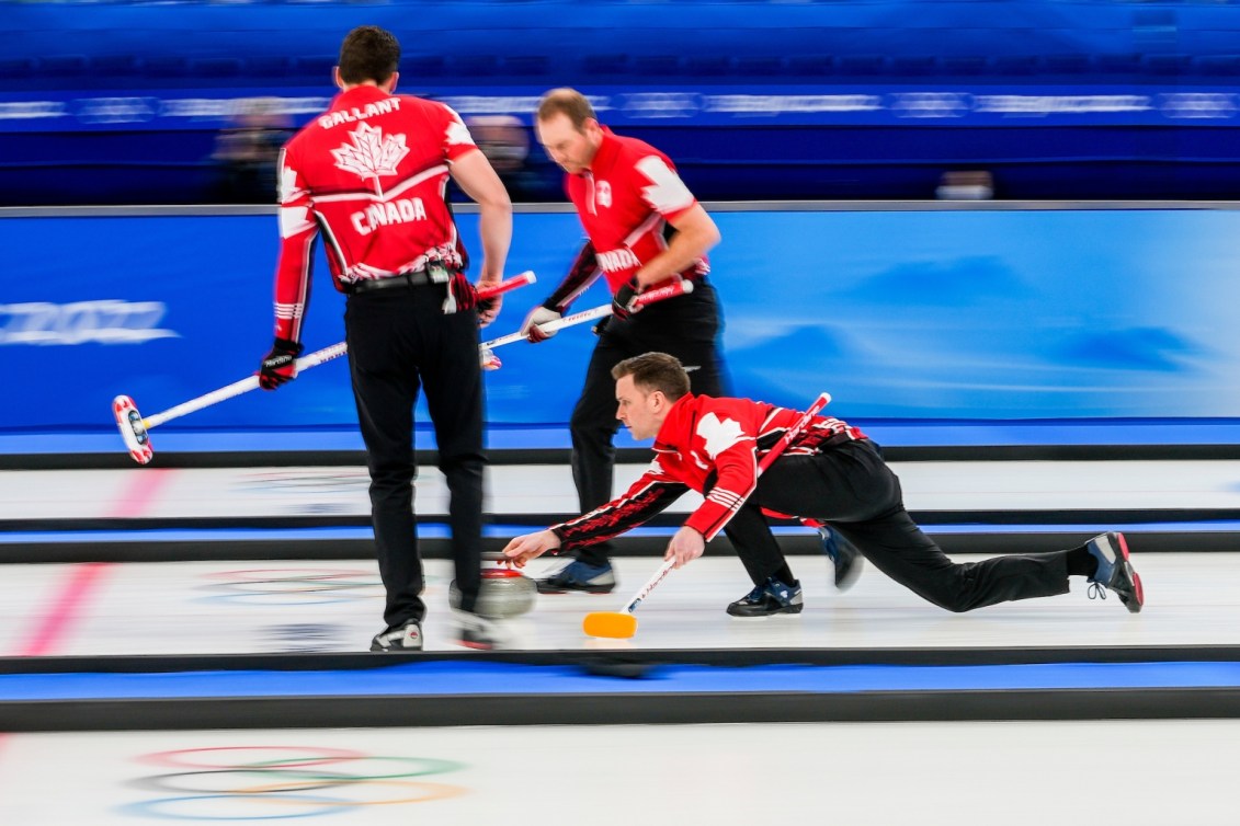 Brad Gushue lance une pierre sur la glace tandis que Brett Gallant et Geoff Walker observent son tir à ses côtés, prêts à balayer, lors du match contre les États-Unis en curling masculin à Beijing 2022.