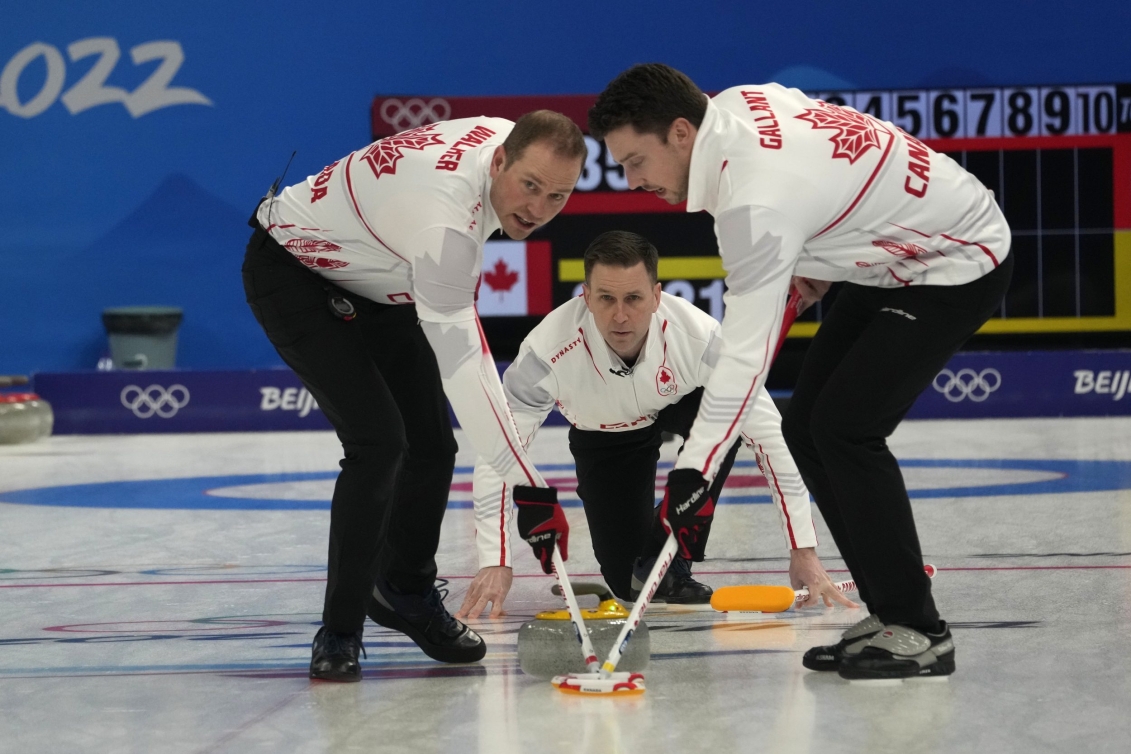 Brad Gushue lance une pierre devant lui tandis que Geoff Walker et Brett Galant balayent la glace pour la faire glisser lors du match de curling contre le Danemark à Beijing 2022