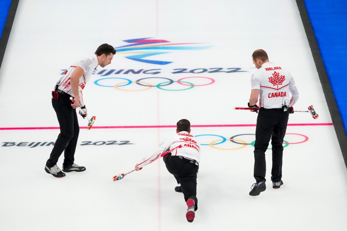 Brad Gushue jette une pierre sur la glace avec ses coéquipiers de chacun de ses côtés lors du match de curling contre la Norvège