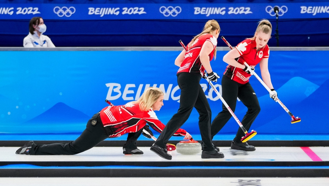 Angle latéral de Jennifer Jones lançant une pierre pour ses deux coéquipières en Curling.