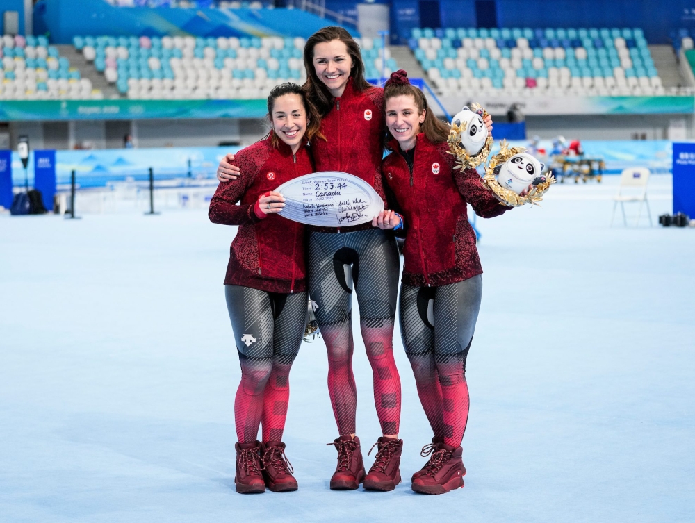 Ivanie Blondin, Isabelle Weidemann et Valérie Maltais se tiennent par les épaules et tendent le résultat de leur temps vers la caméra pour célébrer leur médaille d'or à l'épreuve de poursuite par équipe au patinage de vitesse sur longue piste de Beijing 2022