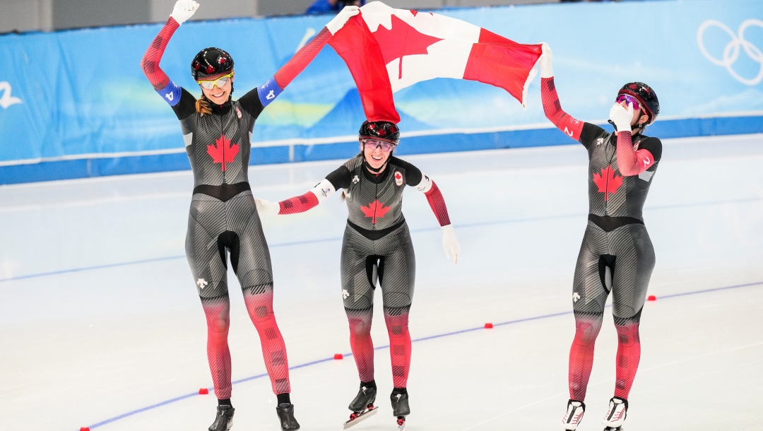 Isabelle Weidemann, Ivanie Blondin et Valérie Maltais agitent le drapeau Canadien dans les airs au-dessus de leurs têtes sur la glace juste après avoir gagné l'or en patinage de vitesse sur longue piste à l'épreuve féminine de poursuite par équipes de Beijing 2022
