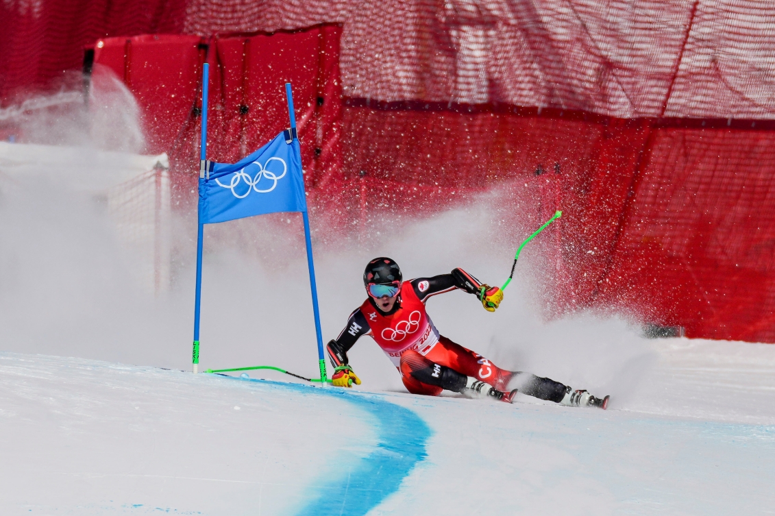 Le skieur alpin canadien Trevor Philp dépasse une porte dans un virage alors que son bassin frôle le sol au super-G masculin de Beijing 2022.