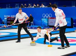 Accroupi sur la glace, Brad Gushue lance une pierre devant lui avec Geoff Walker à sa droite et Brett Gallant à sa gauche qui se préparent à balayer lors du match de curling contre la Suède en demi-finale à Beijing 2022