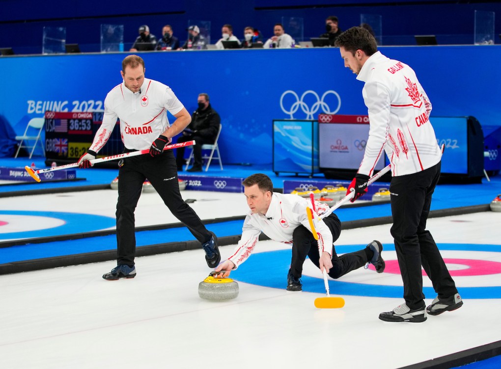 Brad Gushue prend son temps pour viser avant de lancer sa pierre sur la glace alors que Geoff Walker et Brett Gallant patientent à ses côtés pour balayer la glace lors de la demi-finale en curling contre la Suède à Beijing 2022