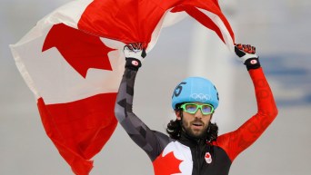 Charles Hamelin brandit le drapeau canadien au-dessus de sa tête.