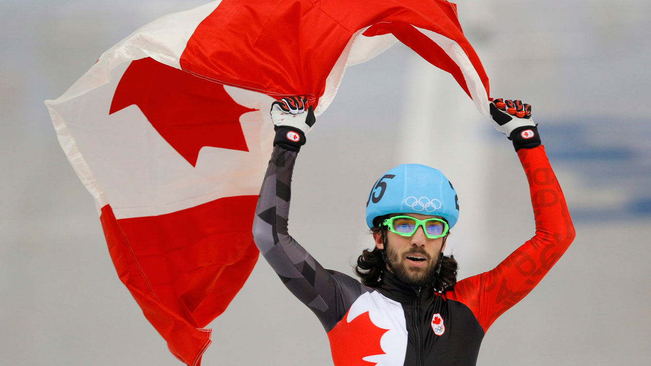 Charles Hamelin brandit le drapeau canadien au-dessus de sa tête.