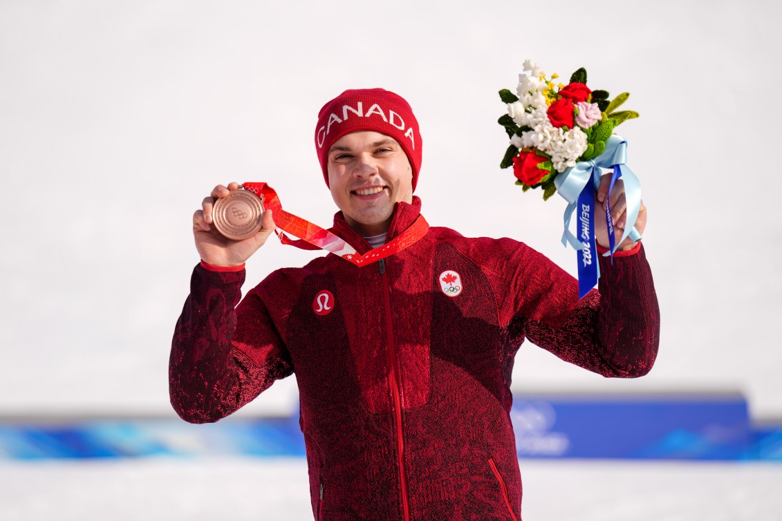 Le skieur alpin d'Équipe Canada Jack Crawford montre sa médaille de bronze avec sa main droite et soulève son bouquet de fleurs sur le podium du combiné alpin masculin à Beijing 2022.