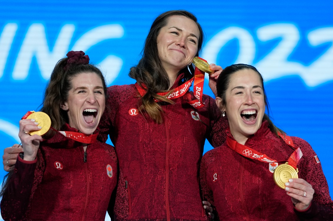 Trois médaillée se prennent par les épaules avec leur médailles d'or autour du cou