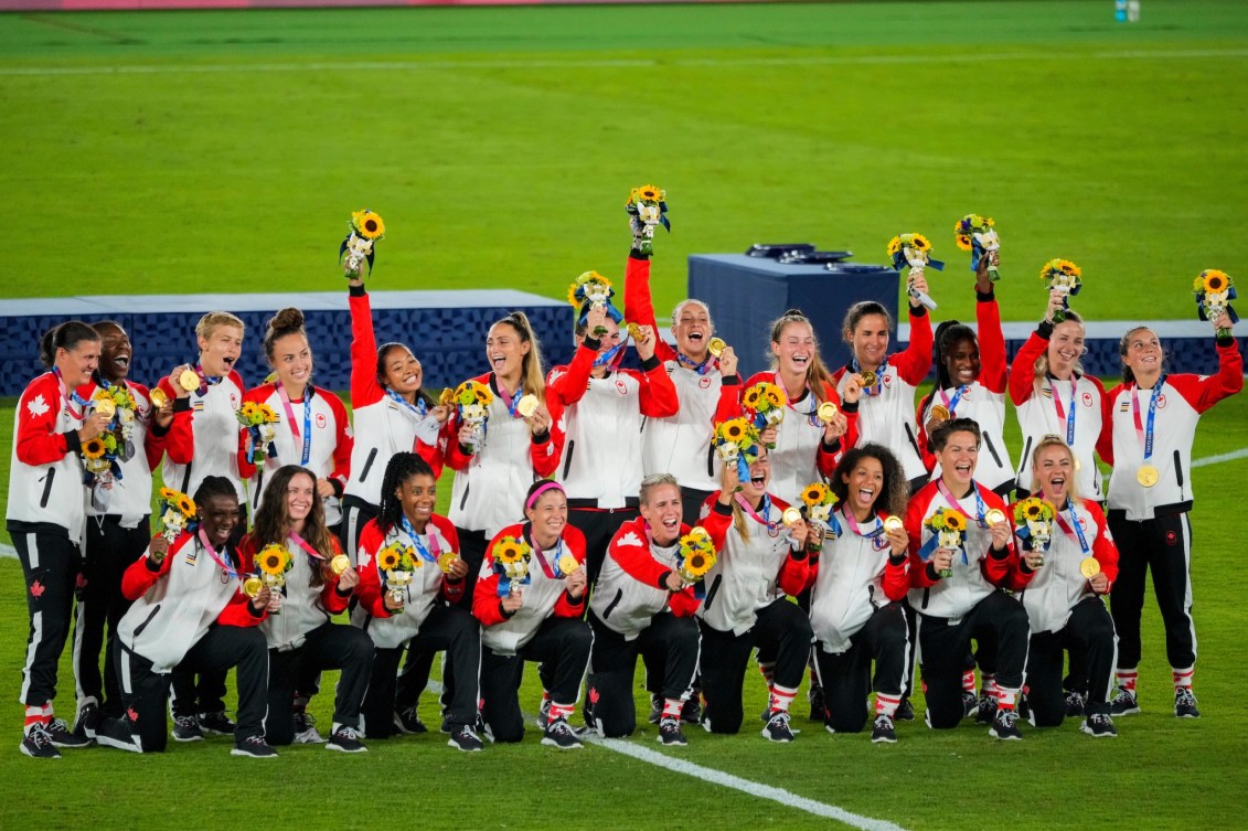 Les membres de l'équipe féminine de soccer sourient, positionnées les unes aux côtés des autres, et lèvent leurs bouquets de fleurs en l'air pour célébrer leur médaille d'or gagnée à Tokyo 2020.