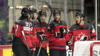 Des joueurs d'Équipe Canada sont adossé à la bande de la patinoire.