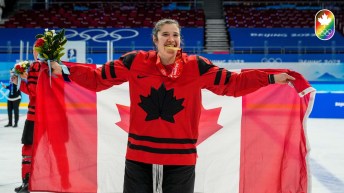 Une femme tient le drapeau canadien derrière elle. Elle mord dans une médaille d'or.