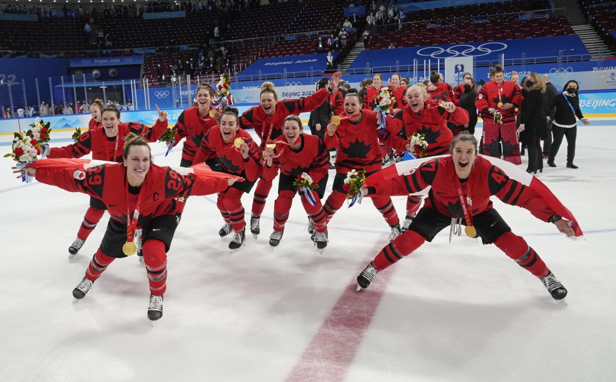 Des joueuses de hockey drapées du drapeau canadien et une médaille d'or au cou. 