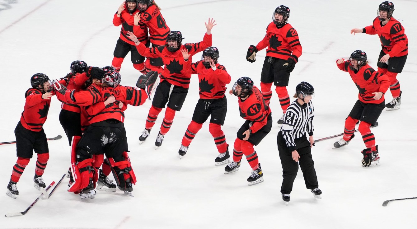 Des joueuses de hockey lèvent les bras dans les airs sur la glace en fin de match. 