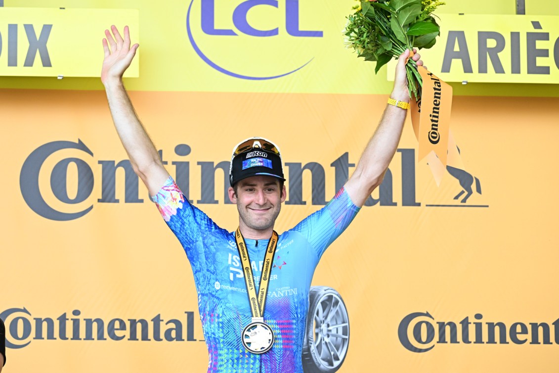 Un cycliste une médaille au cou, les bras dans les airs.