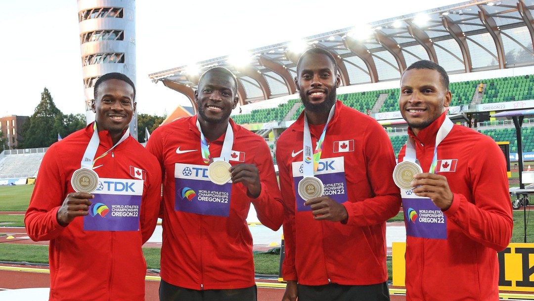 Quatre coureurs avec leur médaille d'or au cou dans le stade d'athlétisme.