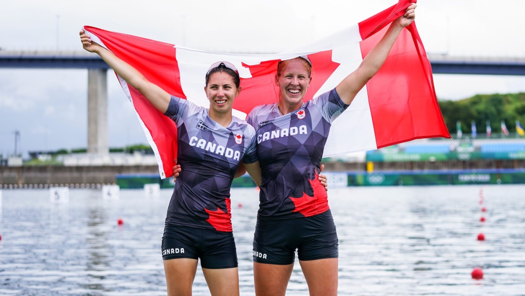 Deux athlètes tiennent un drapeau canadien derrière elles.