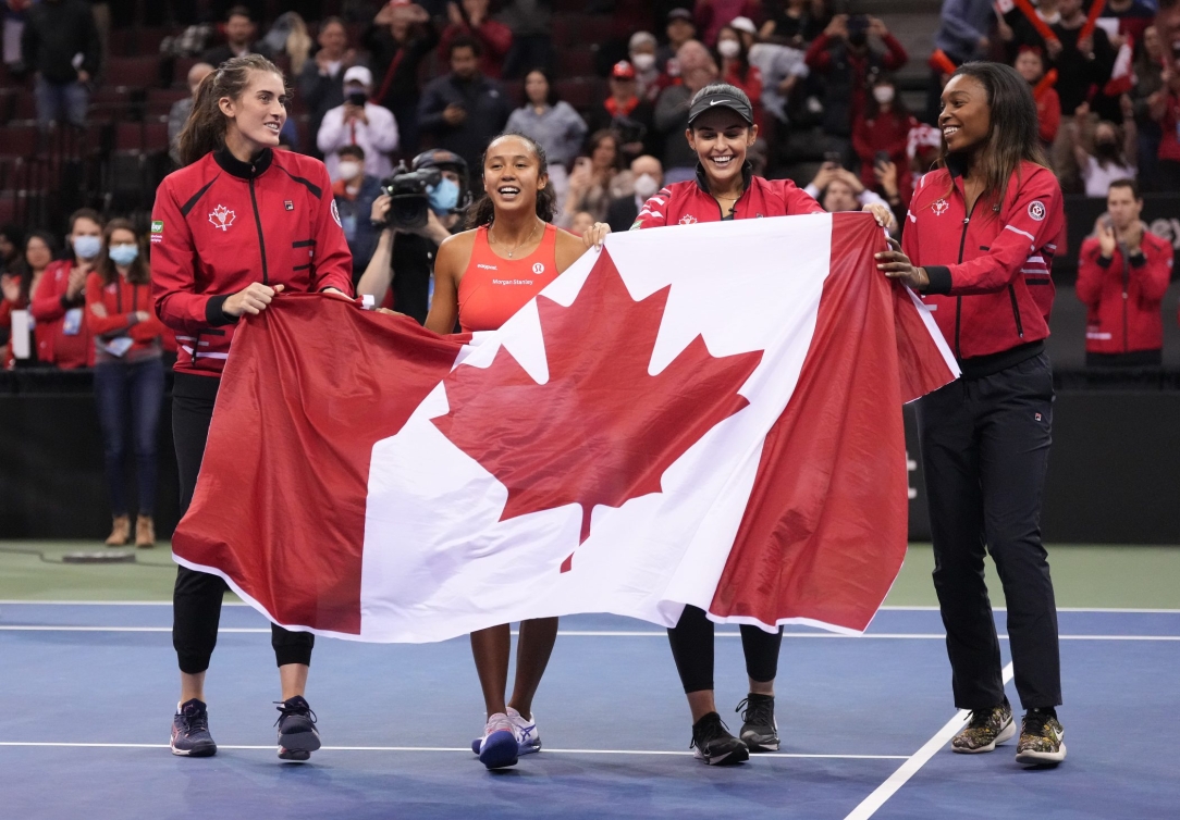 Des femmes tiennent un drapeau canadien devant elles.