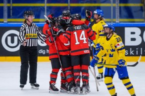 Un groupe d'hockeyeuses canadiennes célèbrent sur la glace. Des joueuse de la Suède sont à côté.