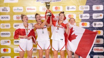 Les joueuses de basketball canadiennes célèbrent avec le trophée et des drapeaux canadien.