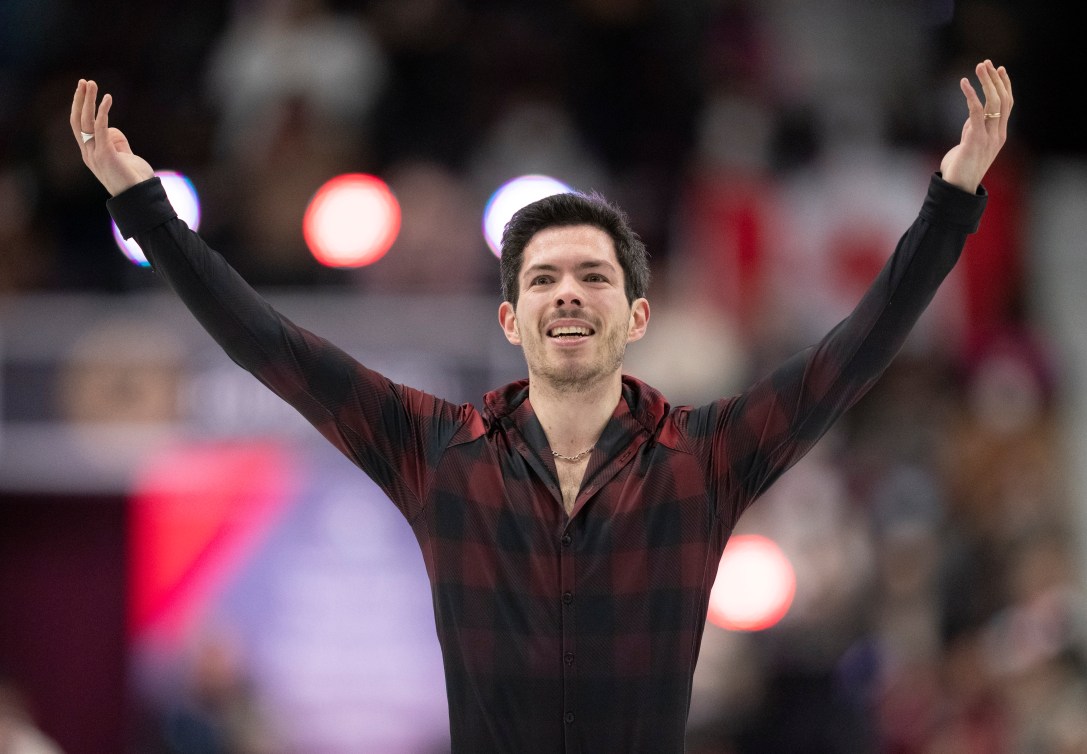 Keegan Messing en chemise à carreaux lève les bras en souriant à la fin de sa performance