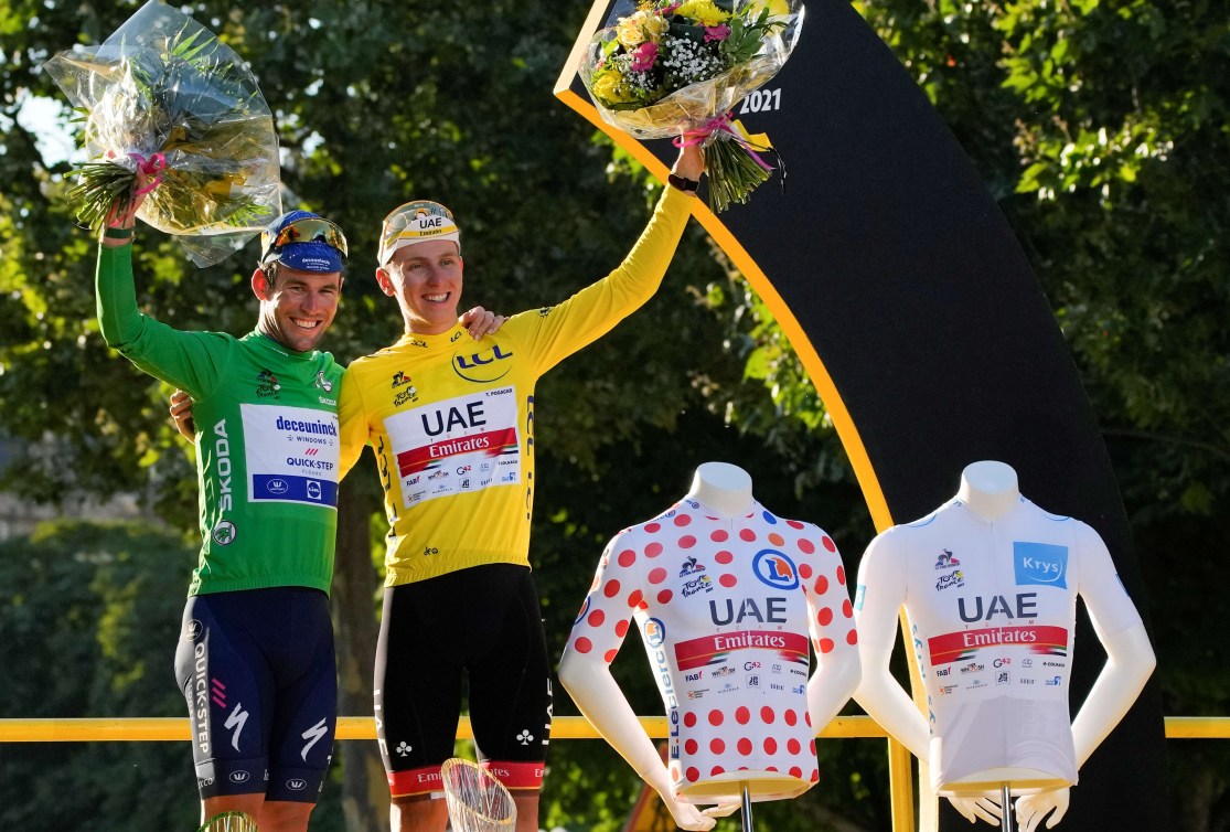 Deux cyclistes lèvent le bras en tenant des fleurs. 