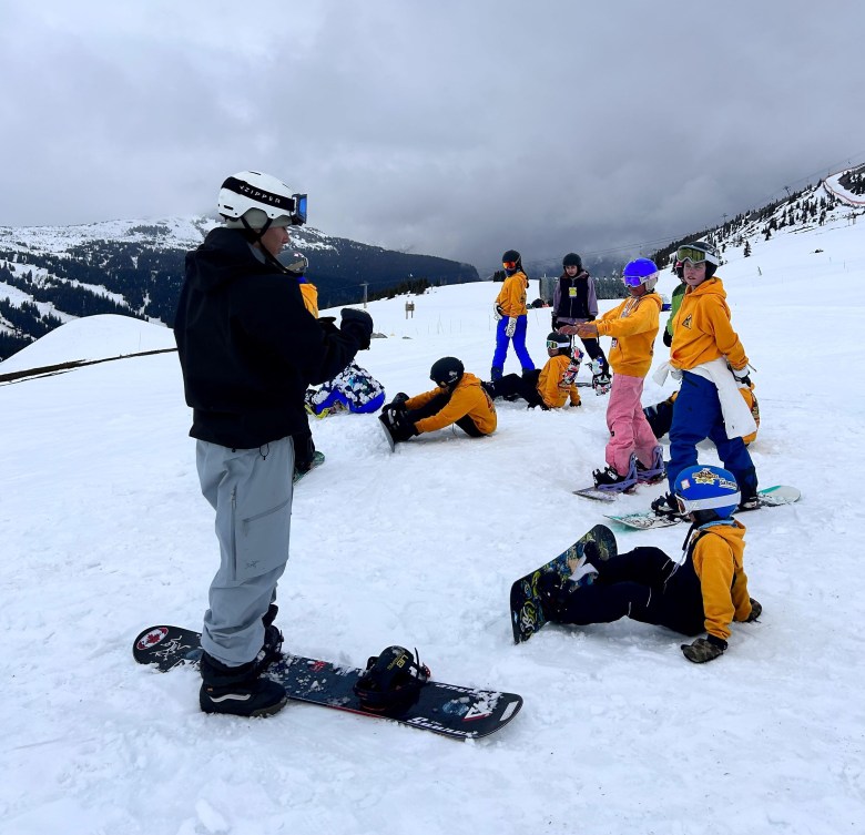 Liam Gill en train de donner des instructions à de jeunes planchistes autochotones, à l'extérieur, sur une montagne enneigée.