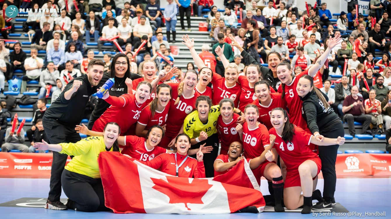 L'équipe féminine canadienne de handball célèbre en posant derrière le drapeau canadien.