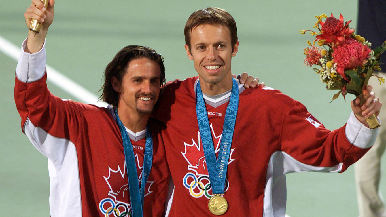 Sébastien Lareau et Daniel Nestor posent avec leur médaille d'or olympique au cou sur le terrain de tennis. 