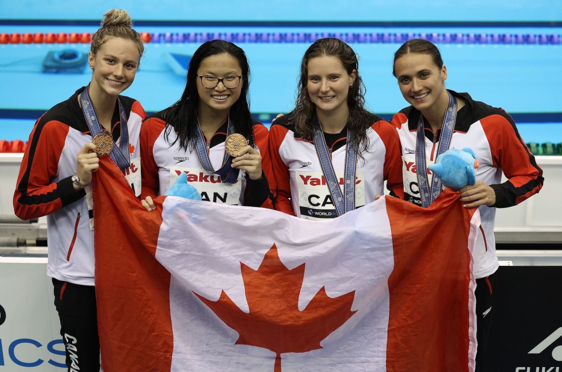 De droite à gauche, Kylie Masse, Sophie Angus, Maggie Mac Neil et Summer McIntosh, avec leur médaille de bronze et un drapeau canadien. 