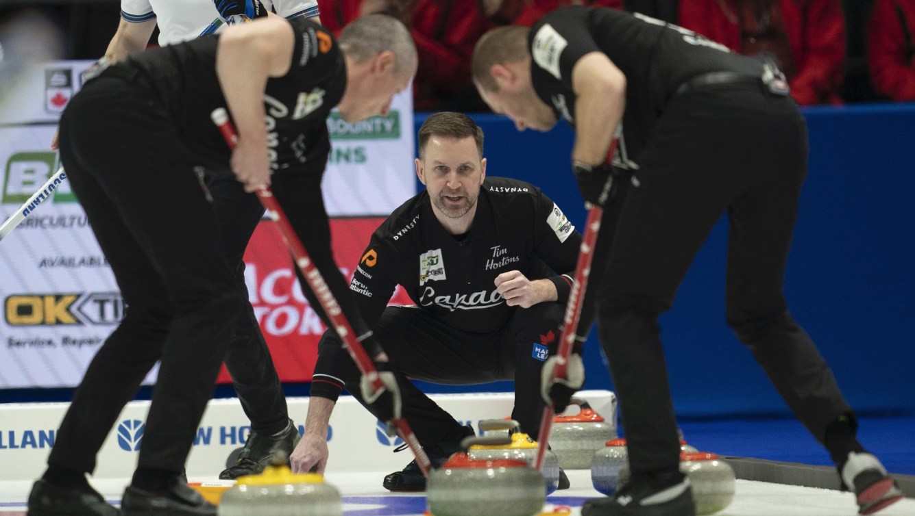 Le skip canadien Brad Gushue observe un lancer se diriger vers la maison tandis que le deuxième EJ Harnden (à gauche) et le premier Geoff Walker balayent.