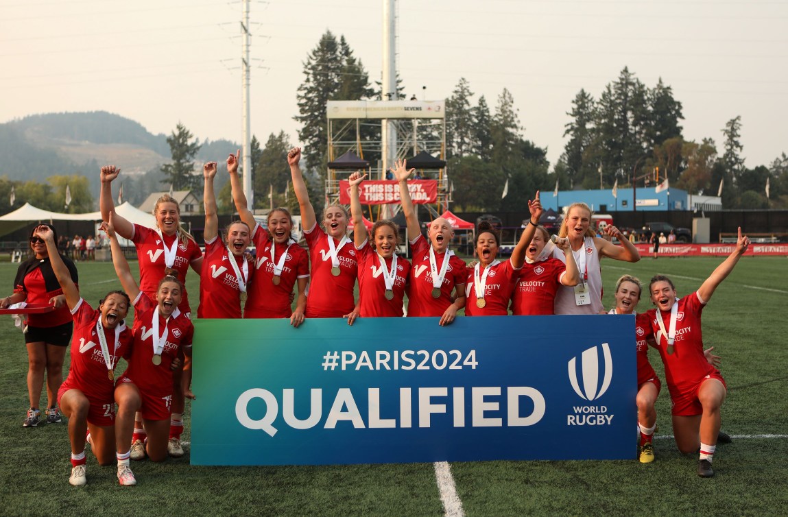 L'équipe féminine de rugby à sept derrière une bannière où il est inscrit «QUALIFIED».