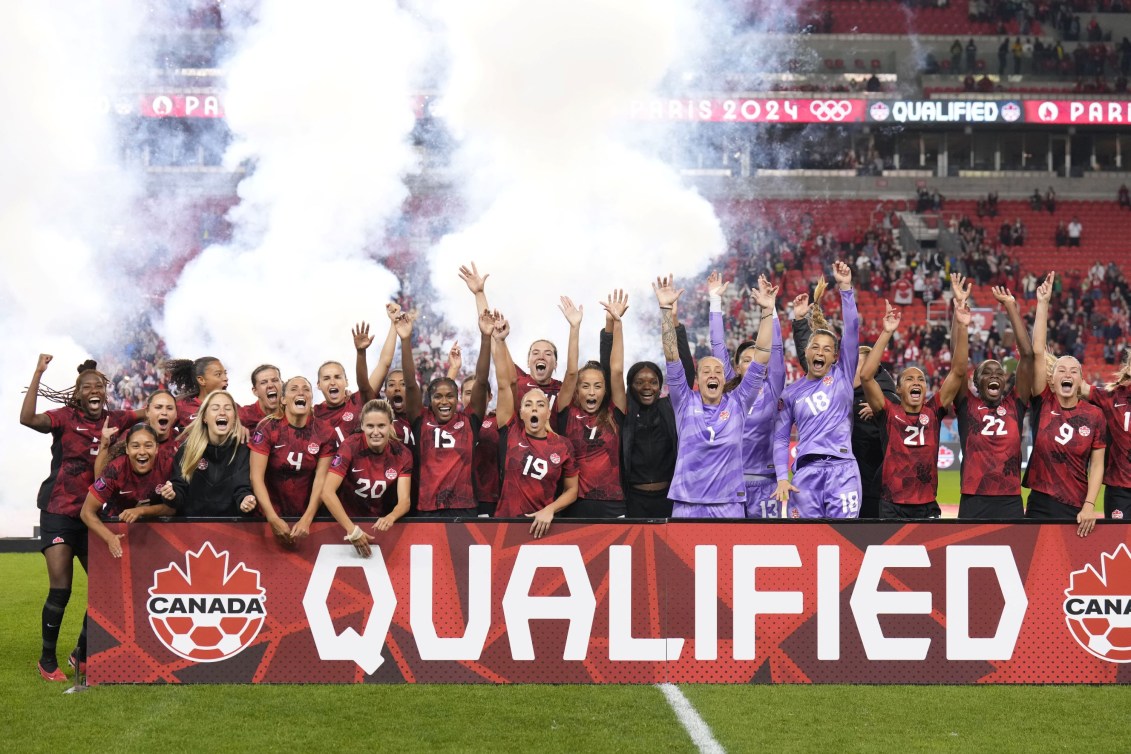 L'équipe féminine de soccer derrière une bannière où il est inscrit «QUALIFIED».