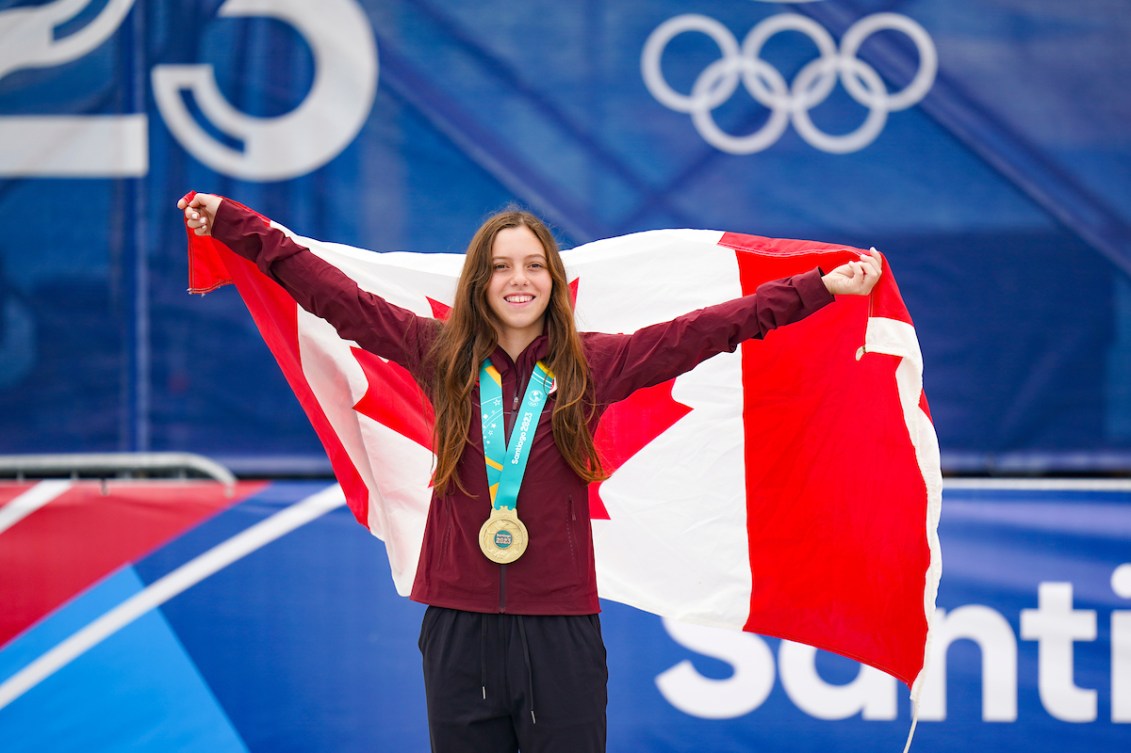 Une athlète une médaille d'or au cou tenant le drapeau canadien. 
