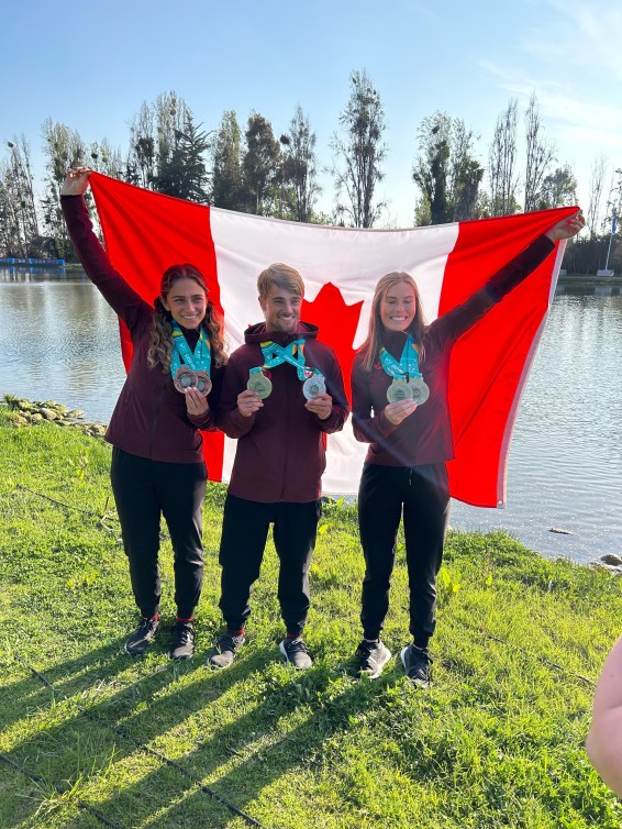 Neilly Ross, Paige Rini et Dorien Llewellyn posent pour une photo avec le drapeau canadien derrière eux.
