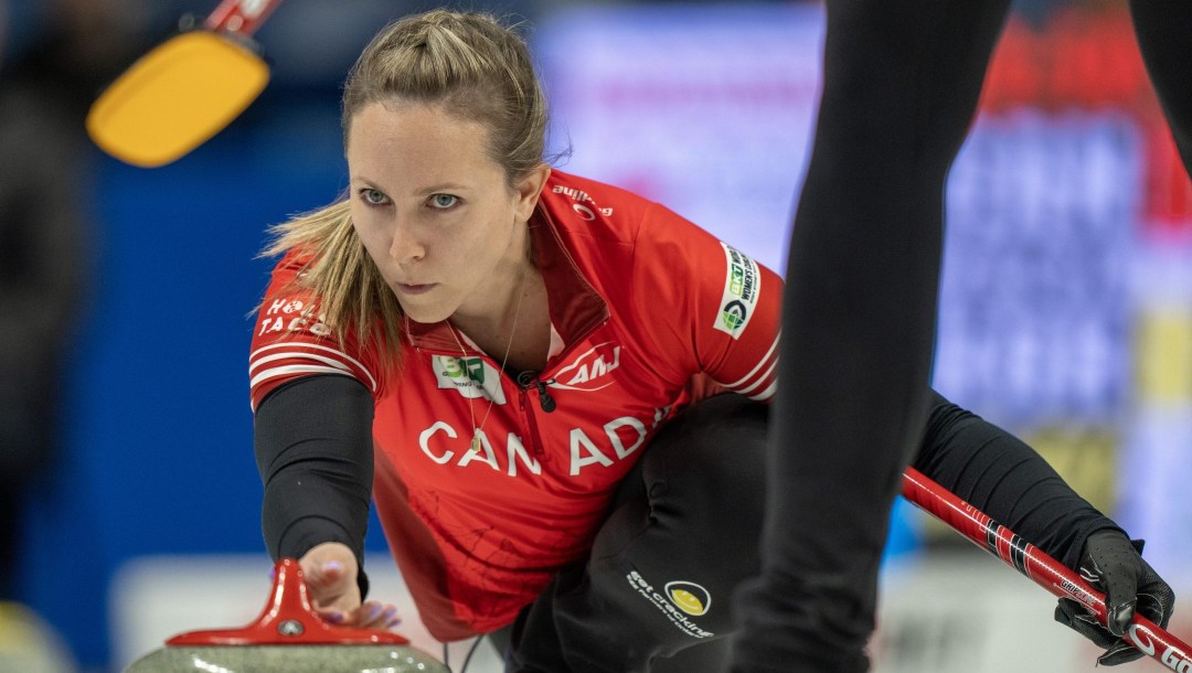 Rachel Homan, accroupit, exécute un lancer au curling.
