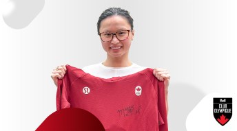 Maggie Mac Neil smiling while holding up a signed sweater