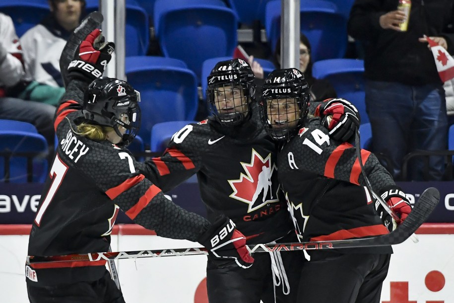 Trois joueuses de l'équipe de hockey féminin du Canada célébrant un but.