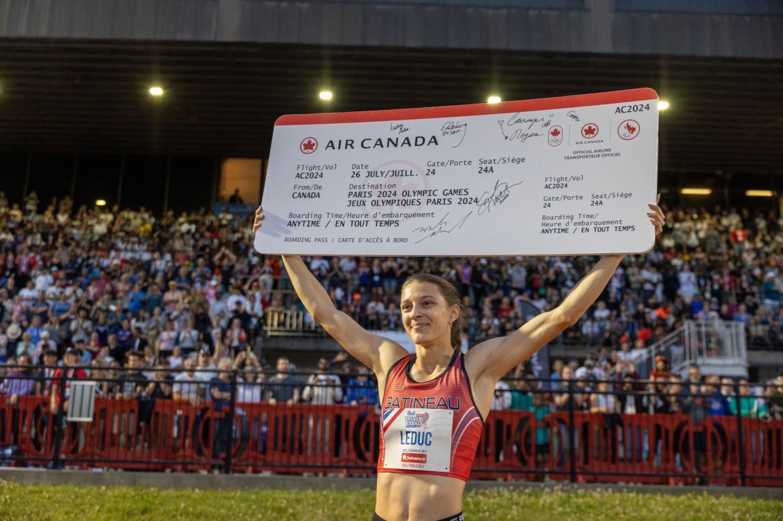 Audrey Leduc tient à bout de bras dans les airs un billet d'avion géant pour Paris 2024.