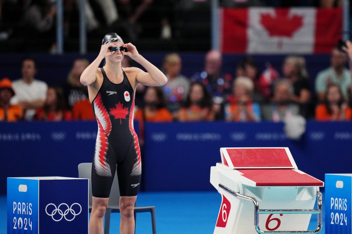 Summer McIntosh stands on the side of the pool and adjusts her goggles