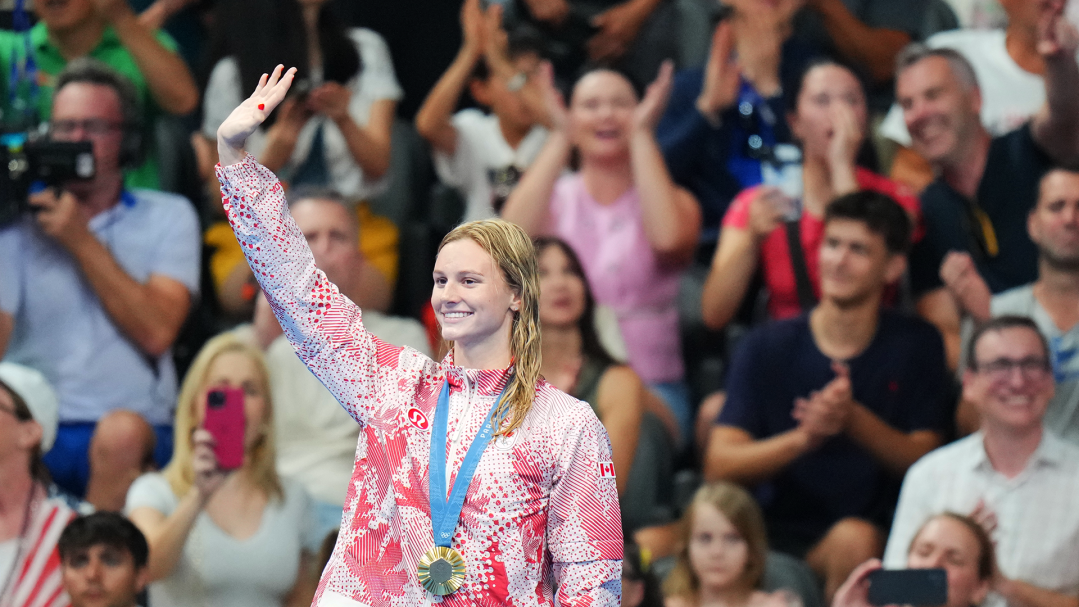 Summer McIntosh salue la foule avec sa médaille d'or au cou.