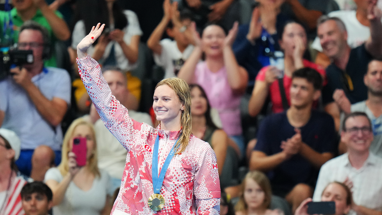 Summer McIntosh salue la foule avec sa médaille d'or au cou. 