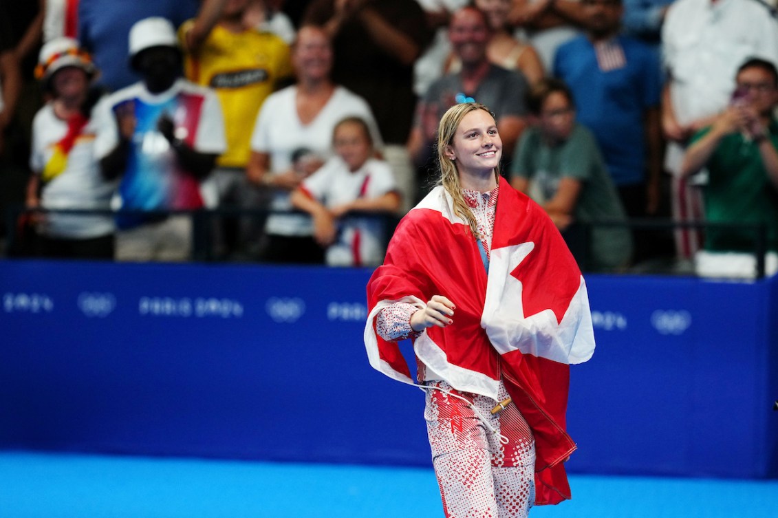 Summer McIntosh célèbre sa médaille d'or enveloppée du drapeau canadien.