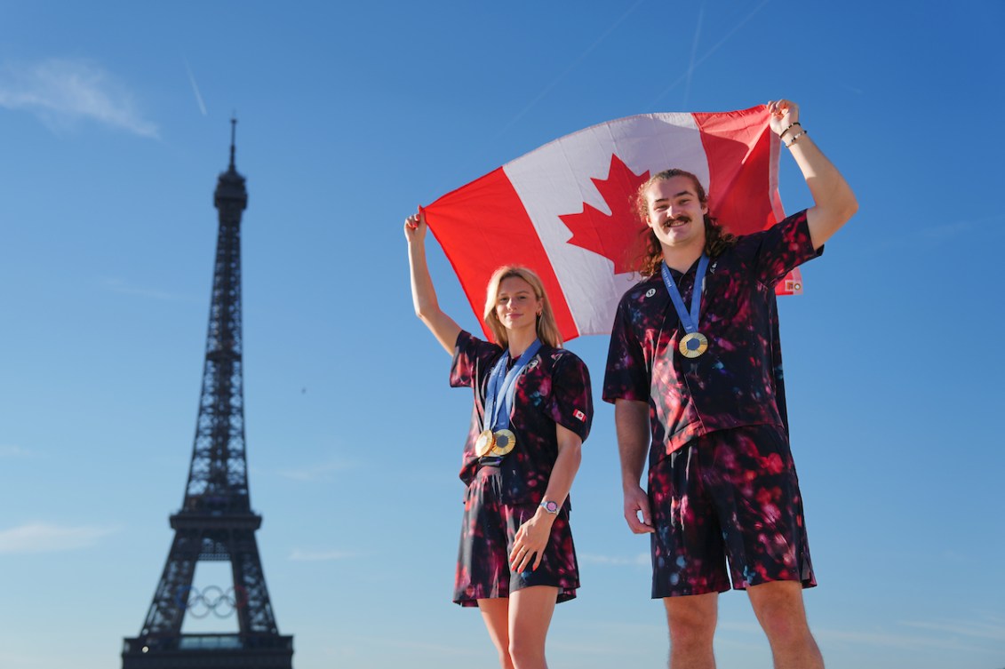 Summer McIntosh et Ethan Katzberg d'Équipe Canada posent devant la tour Eiffel avec un drapeau canadien. 